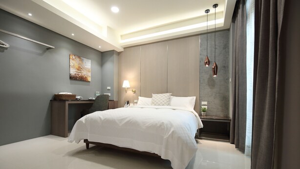 A modern hotel bedroom with a large bed, bedside tables, a desk, and a wall-mounted lamp. - 52Travelers Home (Hualien City)