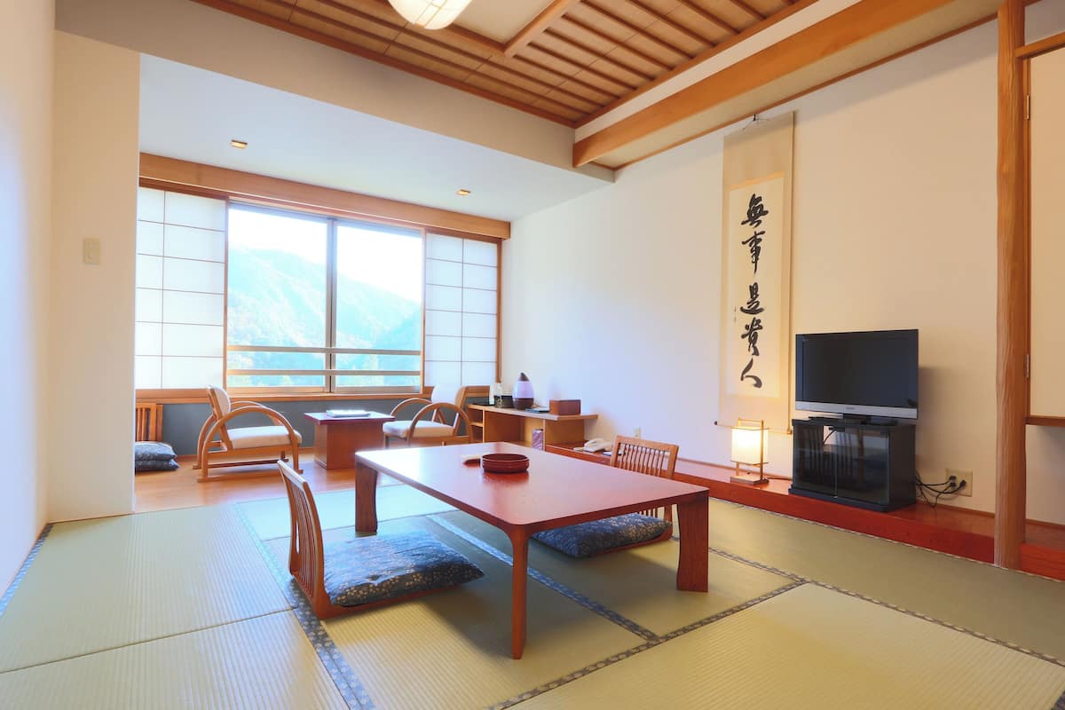 A traditional Japanese-style room with tatami flooring, a low wooden table, and a television on a stand.