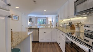 A modern kitchen with white cabinets, granite countertops, stainless steel appliances, and a view to the dining area. - SHIPYARD - WALK TO BEACH & STEPS TO POOL.  Bright corner unit & golf course view (Hilton Head Island)