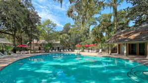 A swimming pool with lounge chairs and umbrellas, surrounded by trees and a building with a tiled roof. - SHIPYARD - WALK TO BEACH & STEPS TO POOL.  Bright corner unit & golf course view (Hilton Head Island)