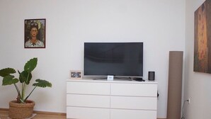 A modern living room with a flat-screen TV on a white cabinet, a potted plant, and a painting on the wall. - Apartment in town centre,beautiful and quiet,ideal for families and couples (Zagreb)
