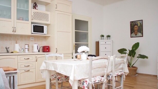 A kitchen with white cabinets, a microwave, and a dining table with floral chairs. - Apartment in town centre,beautiful and quiet,ideal for families and couples (Zagreb)