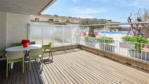 A balcony with a wooden floor, a table with chairs, and a view of a swimming pool and buildings in the background. - APARTMENT 7 ADULTS POOL VIEW (L'Estartit)