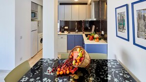 A modern kitchen with white cabinets, a microwave, and a sink. There's a table with a floral tablecloth and a basket of fruit. - APARTMENT 7 ADULTS POOL VIEW (L'Estartit)
