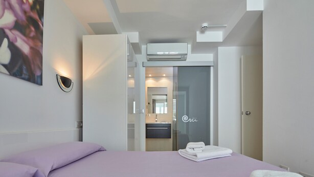 A modern hotel room with a bed, a bathroom visible through a glass door, and an air conditioning unit on the ceiling. - APARTMENT 7 ADULTS POOL VIEW (L'Estartit)