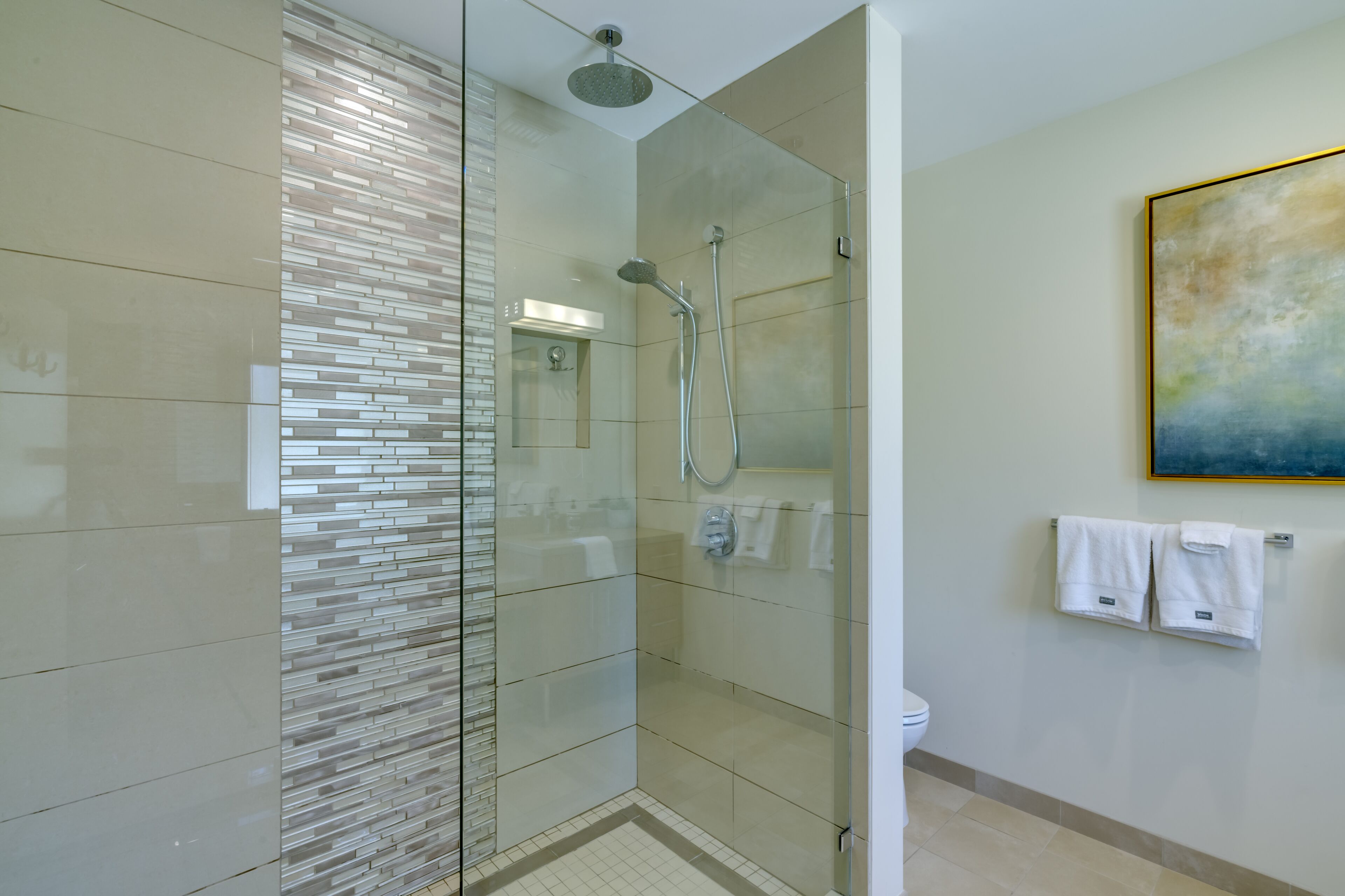 A modern bathroom with a glass-enclosed shower, a toilet, and a towel rack with two towels.