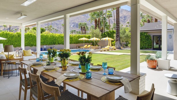 Un vaste espace extérieur aménagé pour les repas, avec vue sur la piscine, des tables disposées avec soin et des sièges confortables.