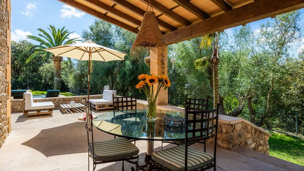 An outdoor patio with a glass table, chairs, a hanging basket, and a stone wall.