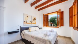 A bedroom with a bed, a nightstand, a wall-mounted shelf, a window with wooden shutters, and a painting on the wall.