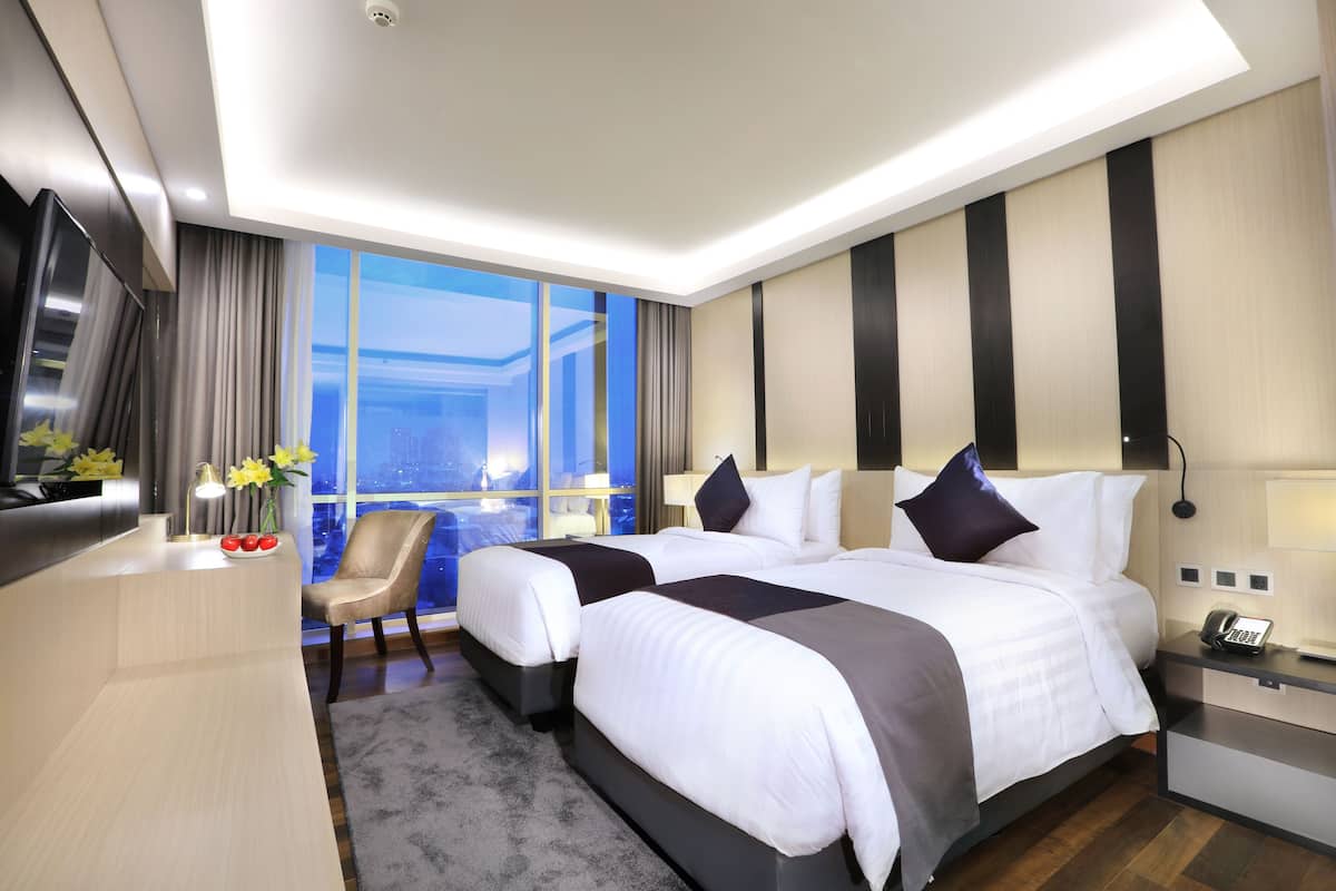 Een moderne hotelkamer met twee bedden, een bureau, een stoel en een groot raam met uitzicht op de stad.