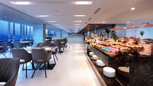 Een moderne hotel lobby met een buffetgedeelte, zithoekjes en een groot raam dat voor natuurlijk licht zorgt.