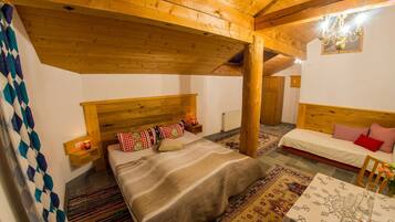 Une pièce chaleureuse avec un grand lit, un plus petit lit, des poutres en bois, une table avec des verres et un tapis à motifs.