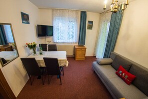 Una habitación con una mesa de comedor, sillas, un sofá, un televisor y una ventana con cortinas.