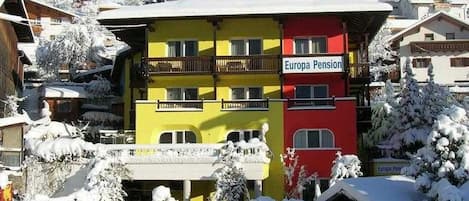 A multi-story building with balconies, labeled 'Europa Pension,' surrounded by snow-covered trees and buildings.