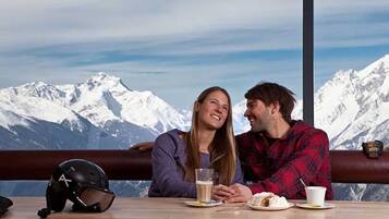 Un couple est assis à une table, avec une vue sur la montagne. Un casque est posé sur la table, ainsi qu’une tasse de café.