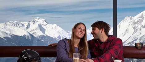 A couple seated at a table with a mountain view, a helmet on the table, and a cup of coffee.