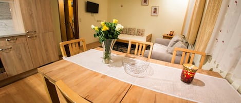 Un comedor con una mesa de madera, sillas, un jarrón con flores y un televisor al fondo.