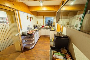 A kitchen with a tiled floor, wooden cabinets, a coffee machine, and a Christmas tree in the background. - Studio for 2- 3 persons - Europa Pension Tirol (Fließ)