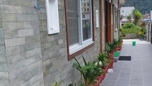 Un edificio con fachada de piedra, una ventana con marco blanco y una hilera de macetas a lo largo del lateral.