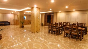 Un lobby espacioso con piso de mármol, pilares de madera, una recepción y un comedor con mesas y sillas de madera.