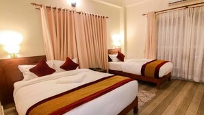 Habitación de hotel con dos camas, cortinas color beige, piso de madera y una mesita de noche con lámpara.