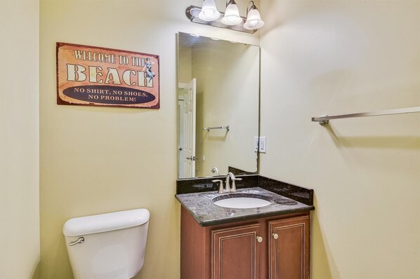 A bathroom with a toilet, sink, and wooden cabinets. A sign above the sink reads "Welcome to the Beach, No Shirt, No Shoes, No Problem!" - Seaclusion A - Ocean Front 5,000sq foot Luxury 8 bedroom duplex w/Pool (NORTH MYRTLE BEACH)