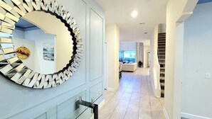 A hallway with a large mirror, a staircase, and a living area in the background. - Voluminous * 5 Bd Pool/Spa Home in Champions Gate (Davenport)