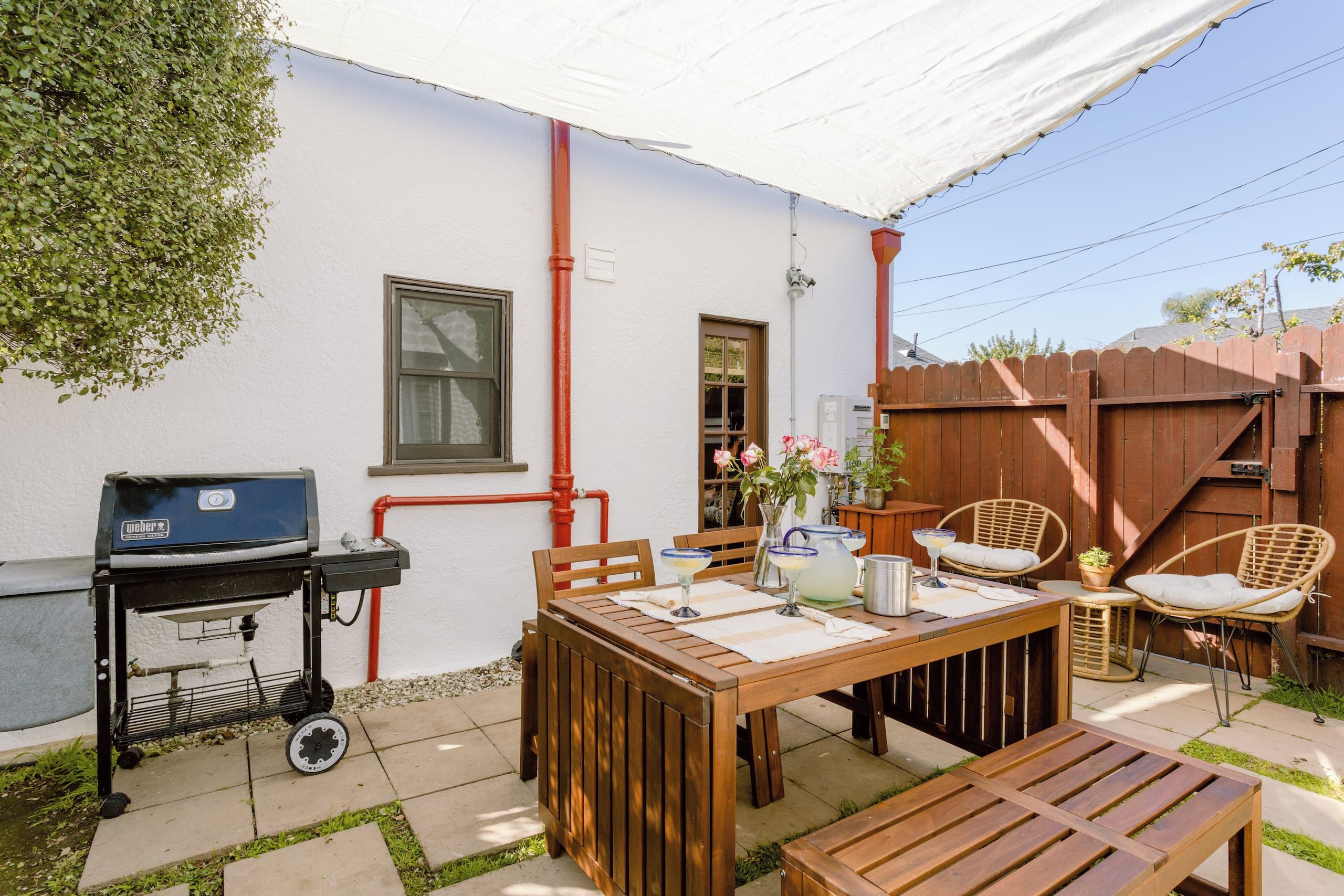 Un patio al aire libre con mesa de madera, sillas, una parrilla y un paraguas blanco.