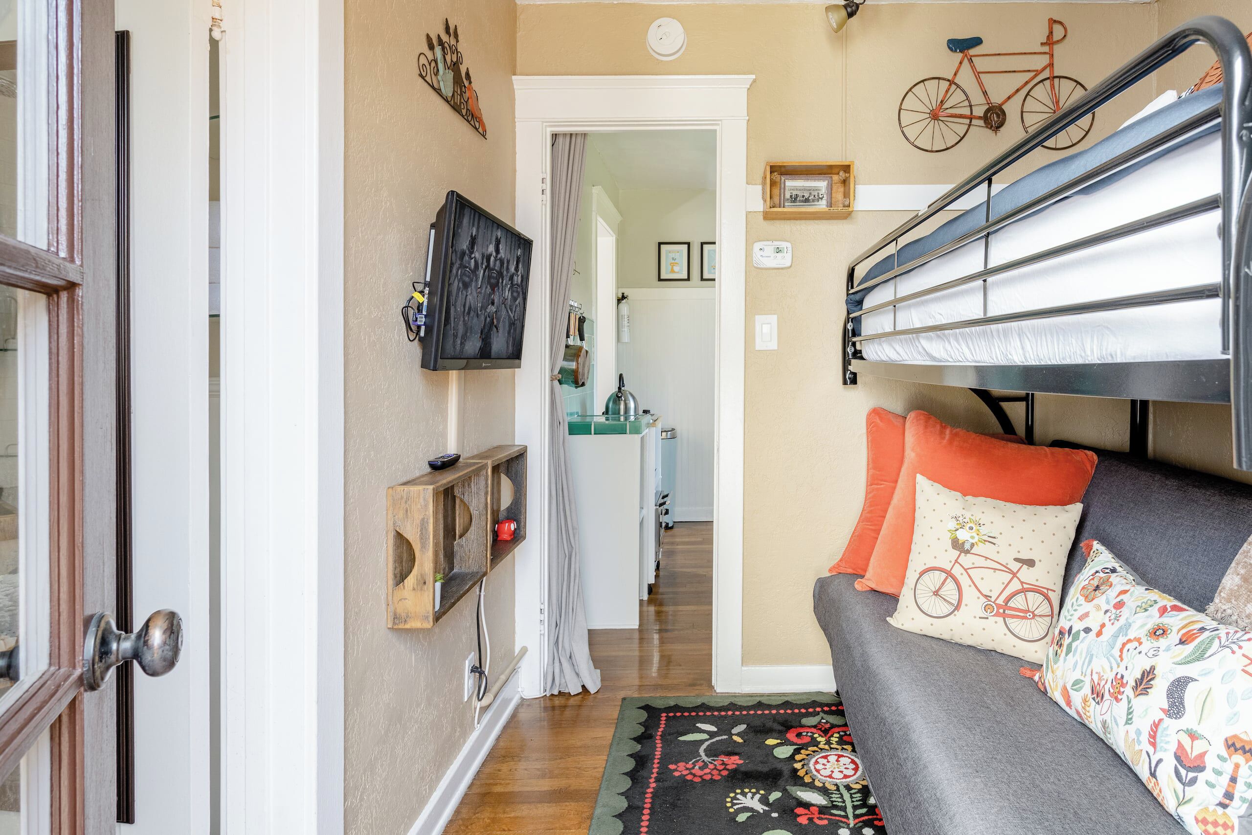 A cozy room with a bunk bed, a sofa with patterned cushions, a wooden shelf with decorative items, and a bicycle wall art piece.