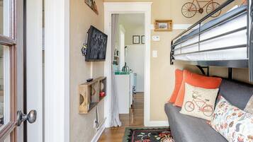 A cozy room with a bunk bed, a sofa with patterned cushions, a wooden shelf with decorative items, and a bicycle wall art piece.