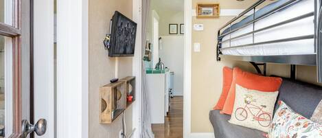 Una habitación acogedora con una cama litera, un sofá con cojines estampados, un estante de madera con objetos decorativos y una obra de arte de bicicleta en la pared.