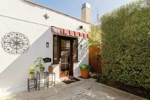 Un edificio blanco con una puerta marrón, plantas en macetas y un adorno metálico en la pared.