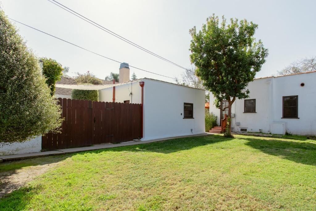Una propiedad residencial con patio cercado, un árbol y un edificio blanco con chimenea.