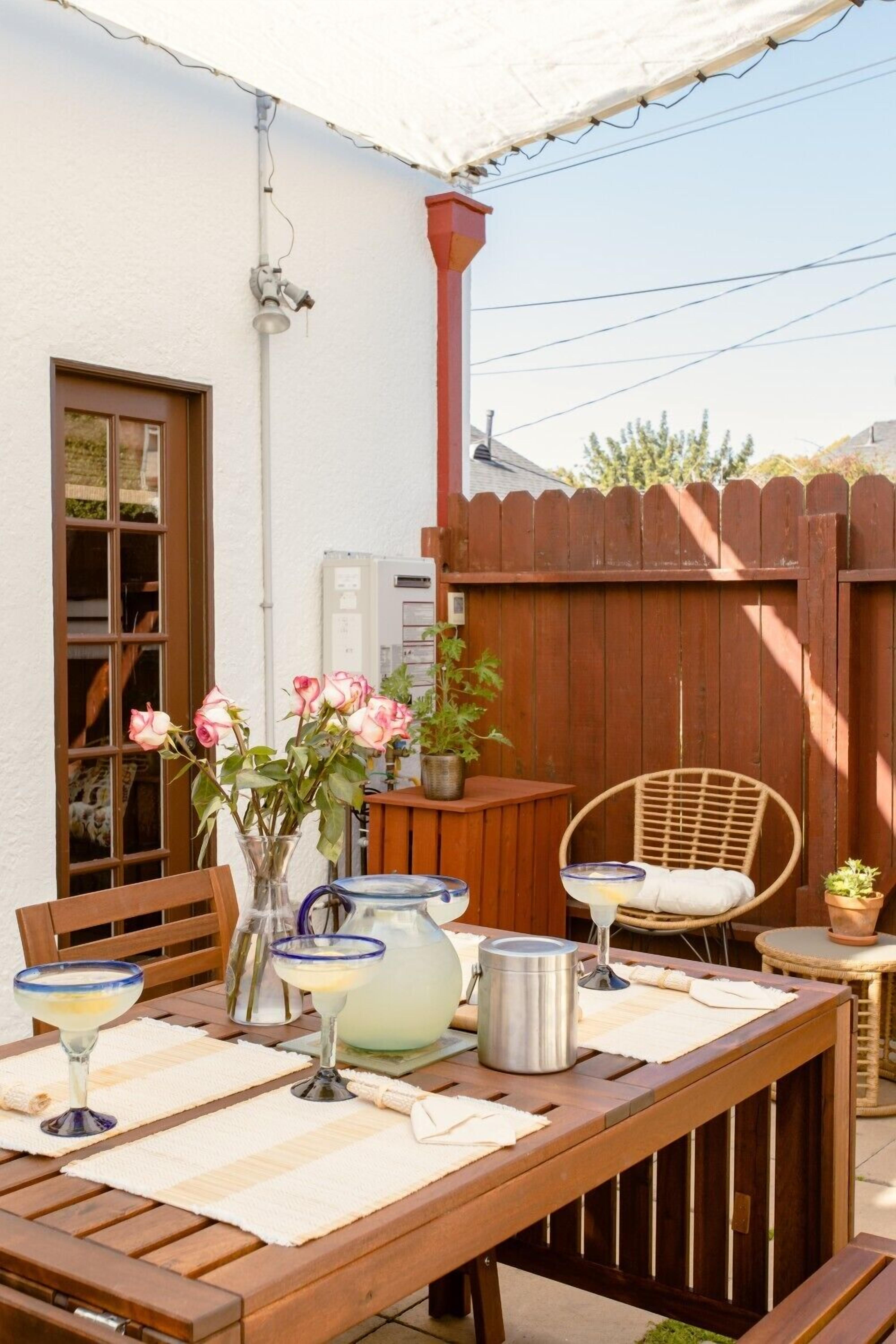 A wooden table set with a pitcher, glasses, and a vase with flowers.