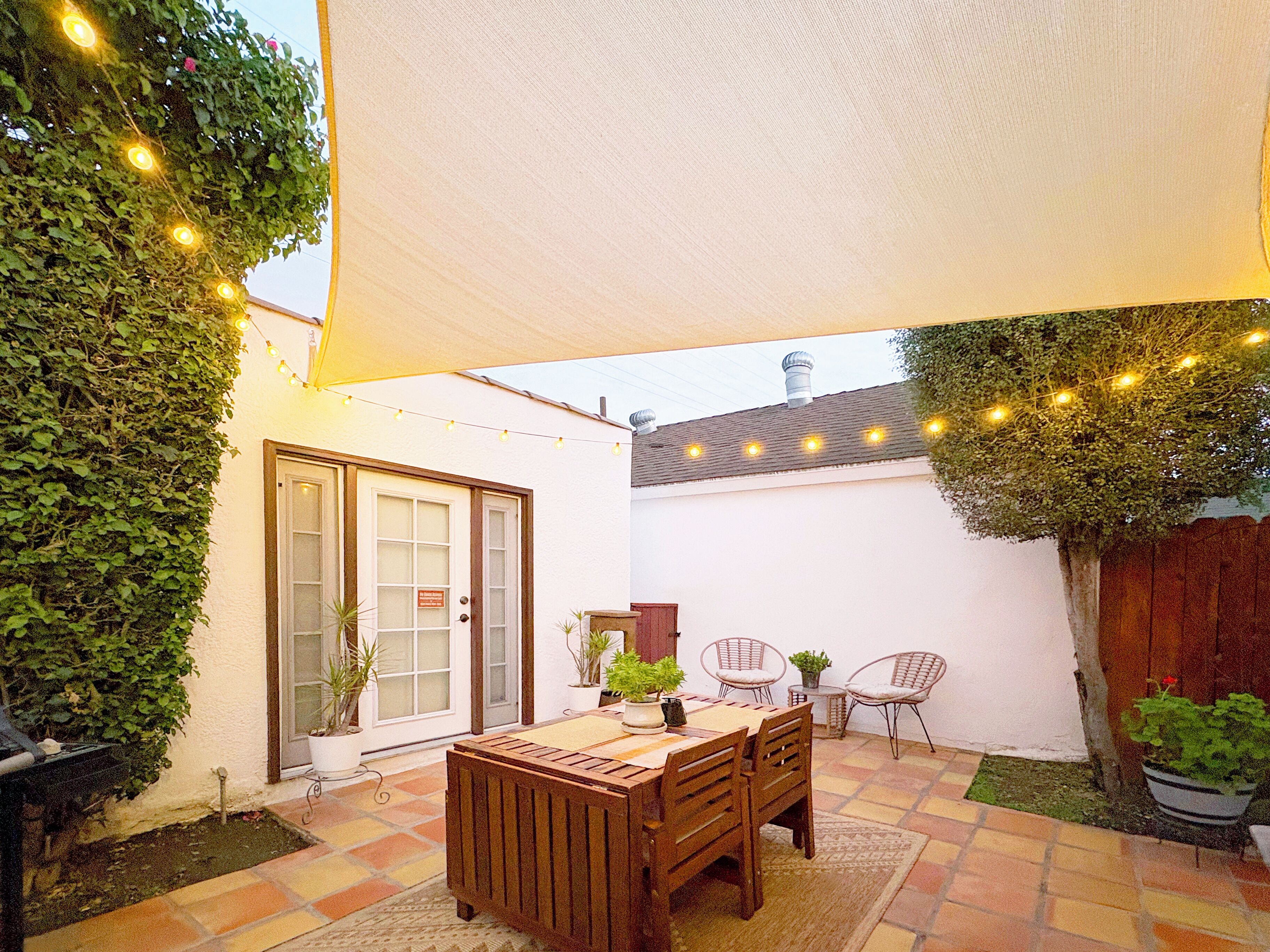 Eine Terrasse mit Holztisch und -stühlen, umgeben von Topfpflanzen und einer weißen Mauer.