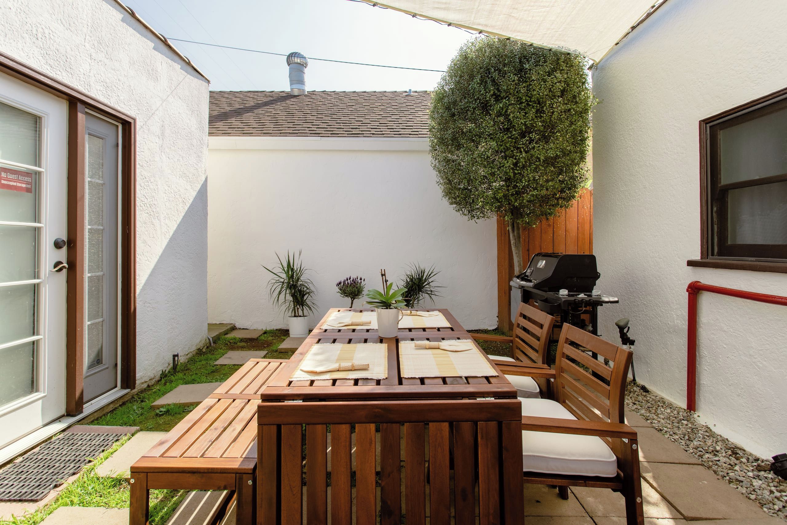 A patio with a wooden table and chairs, a grill, and potted plants.