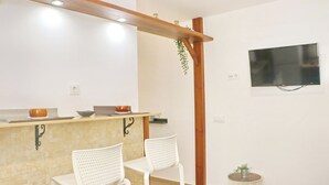A kitchen with a wooden beam ceiling, two white chairs, a small table, and a TV mounted on the wall.