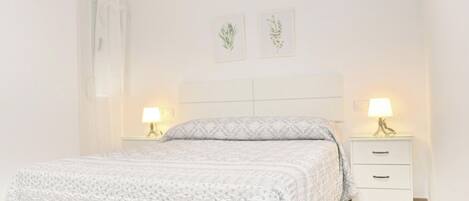 Quarto com cama, duas mesas de cabeceira e duas luminárias na parede.
