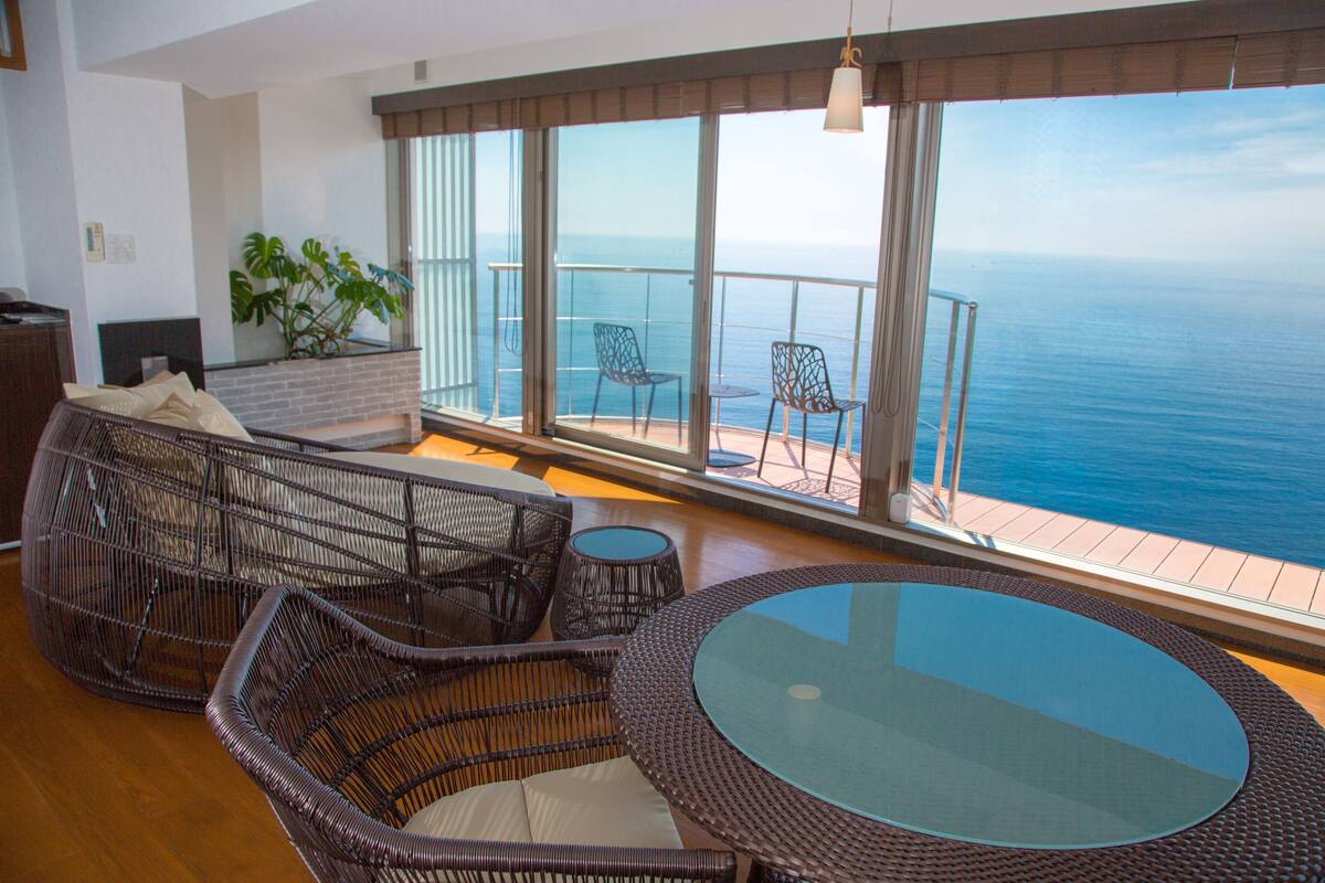 A balcony with wicker furniture, a glass table, and a view of the ocean.