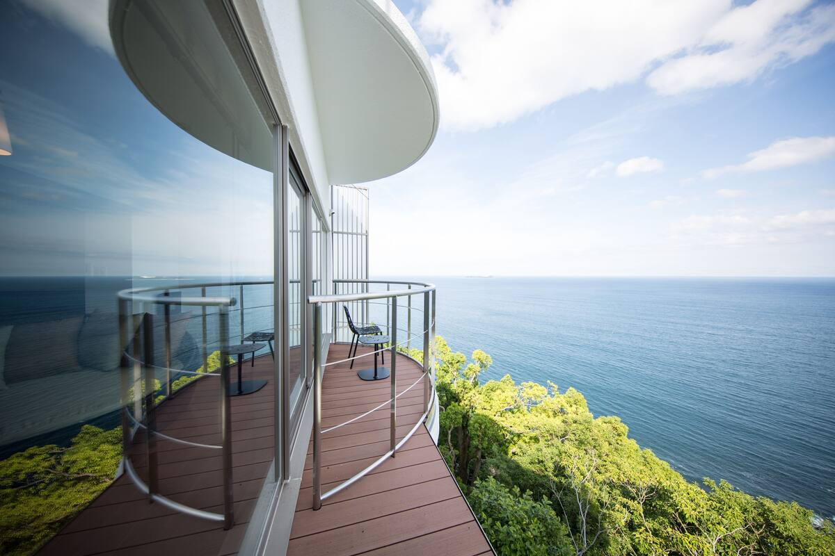 A modern balcony with a glass railing overlooking a body of water and greenery.