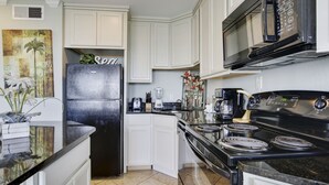 A modern kitchen with white cabinets, a black refrigerator, a microwave, and a stove. - NEW LISTING Day Break at SeaScape #2219: A Place to Rest, Relax, and Rejuvenate! (Galveston)