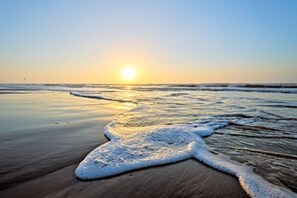 Une plage au coucher du soleil, avec des vagues et un rivage sablonneux.