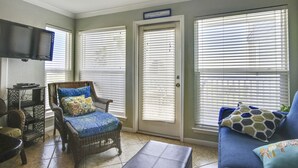A living room with a wicker chair, a blue sofa, and a television mounted on the wall. - NEW LISTING Day Break at SeaScape #2219: A Place to Rest, Relax, and Rejuvenate! (Galveston)