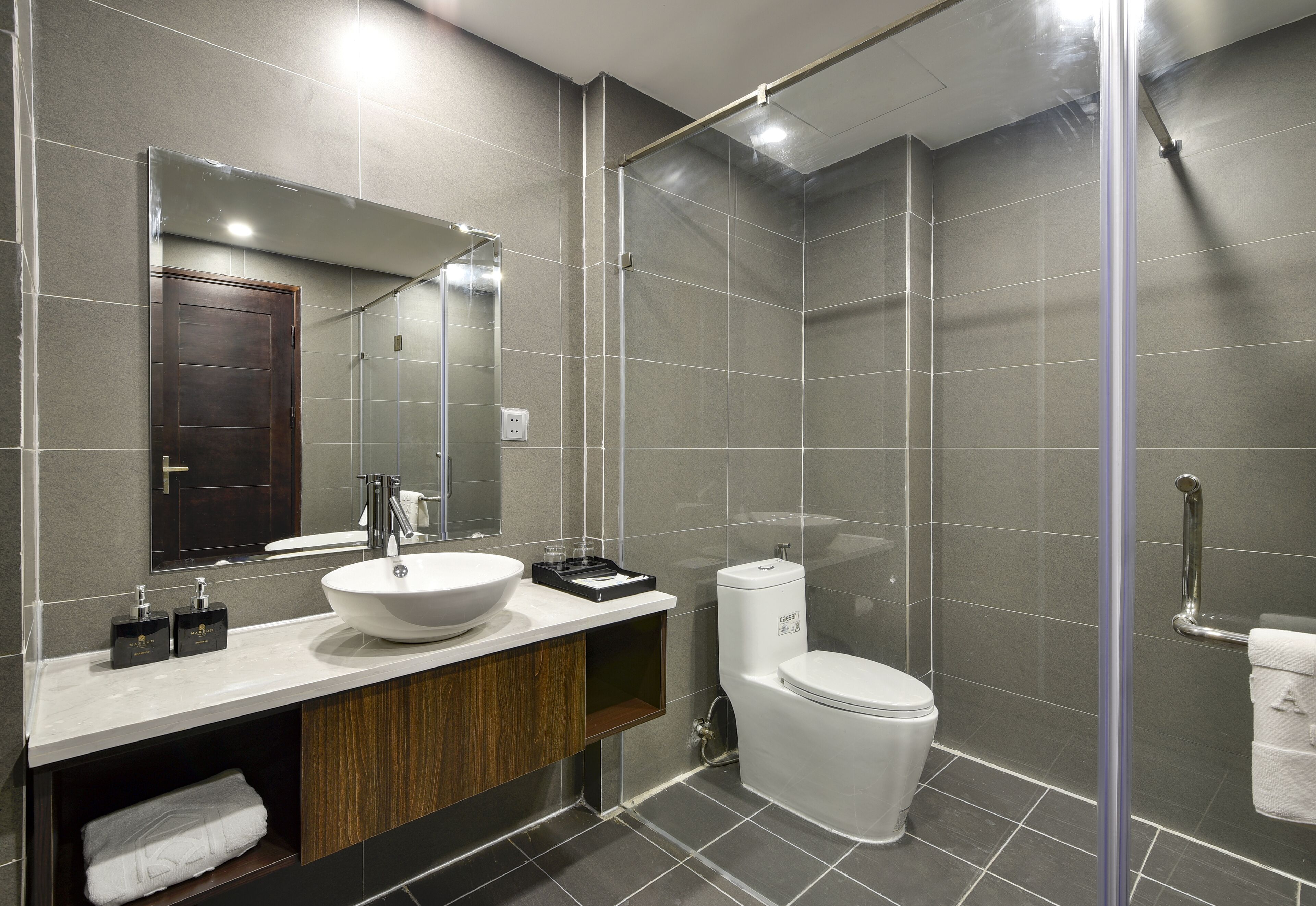 A modern bathroom with a large mirror, a white sink, a toilet, and a shower area.
