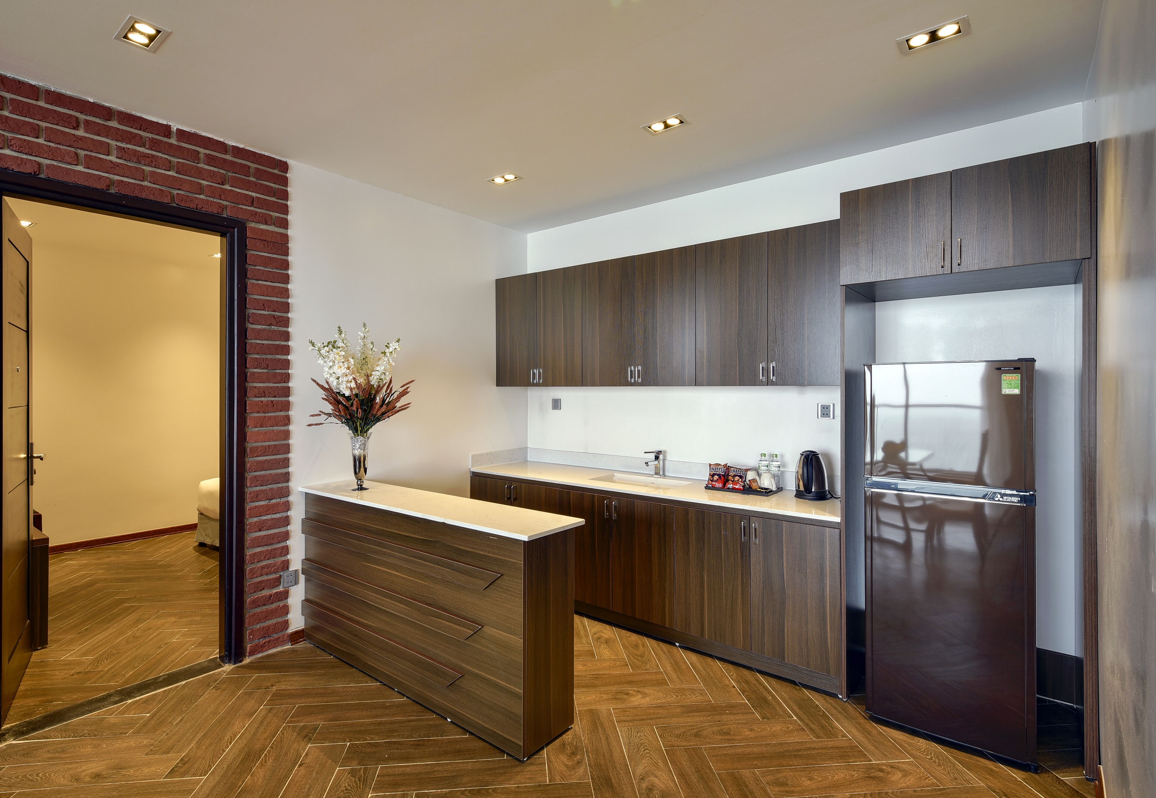 A modern kitchen with wooden cabinets, a stainless steel refrigerator, and a herringbone wood floor.