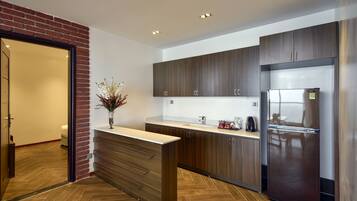 A modern kitchen with wooden cabinets, a stainless steel refrigerator, and a herringbone wood floor.