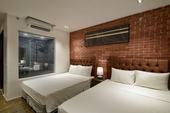 Une chambre d’hôtel avec deux lits, une douche en verre, un mur en briques et un luminaire moderne.