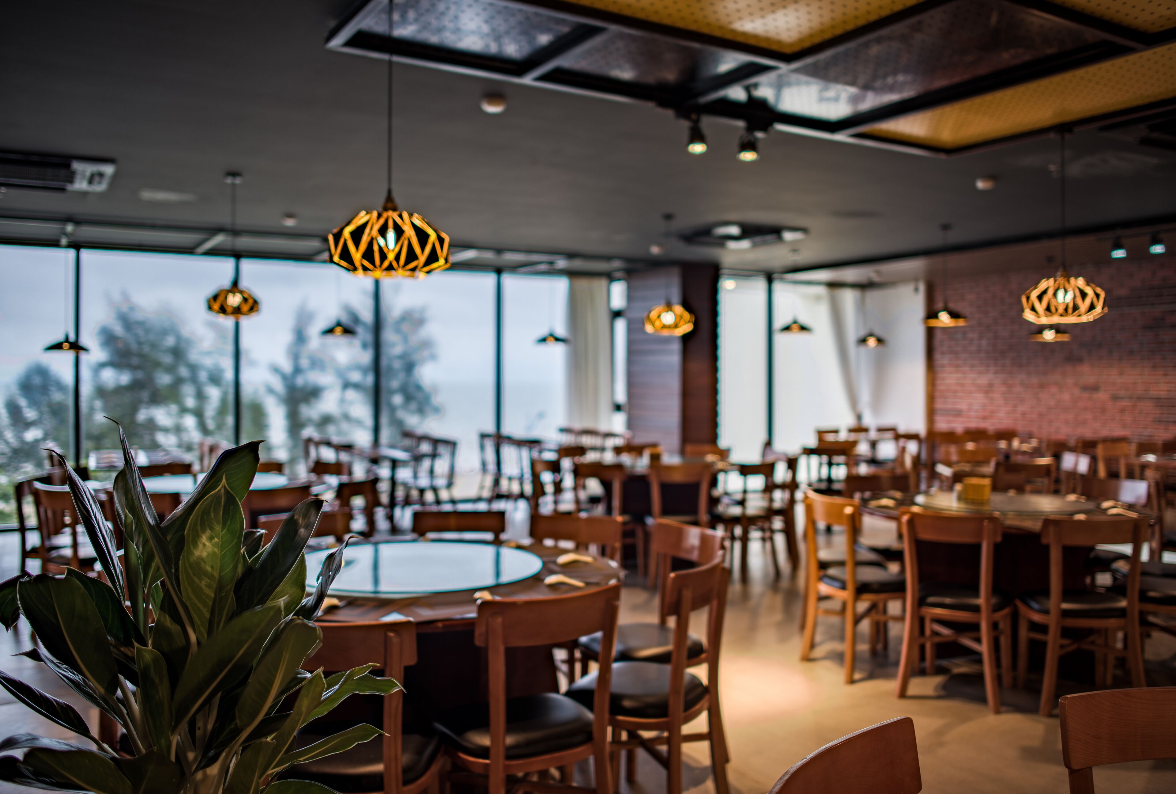 A spacious dining area with multiple tables and chairs, large windows, and hanging pendant lights.