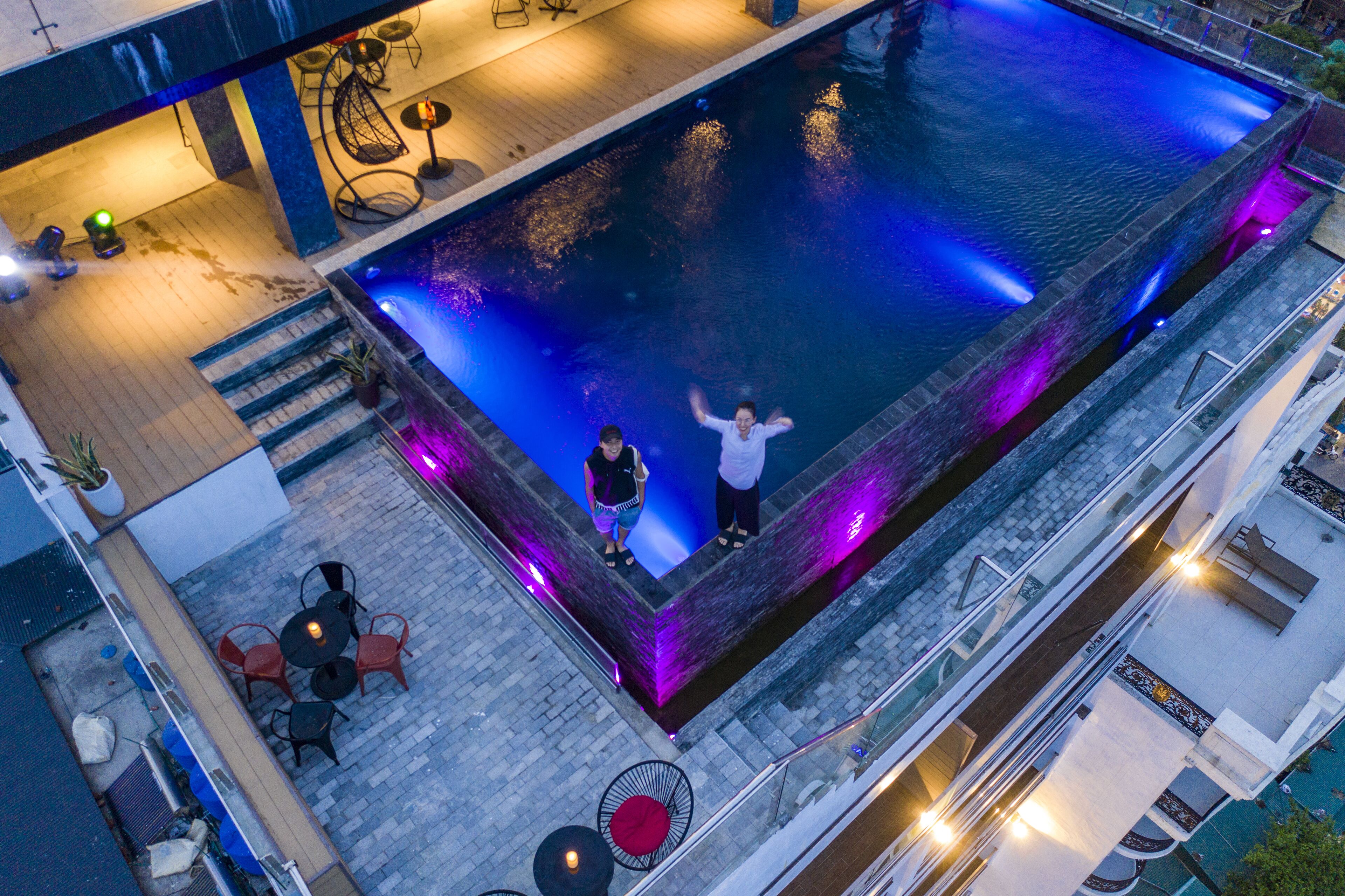 An indoor swimming pool with a stone border, surrounded by outdoor seating and a staircase leading to an upper level.