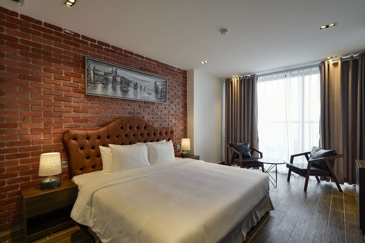 A hotel room with a brick wall, a large bed, a headboard, a desk, and a chair.